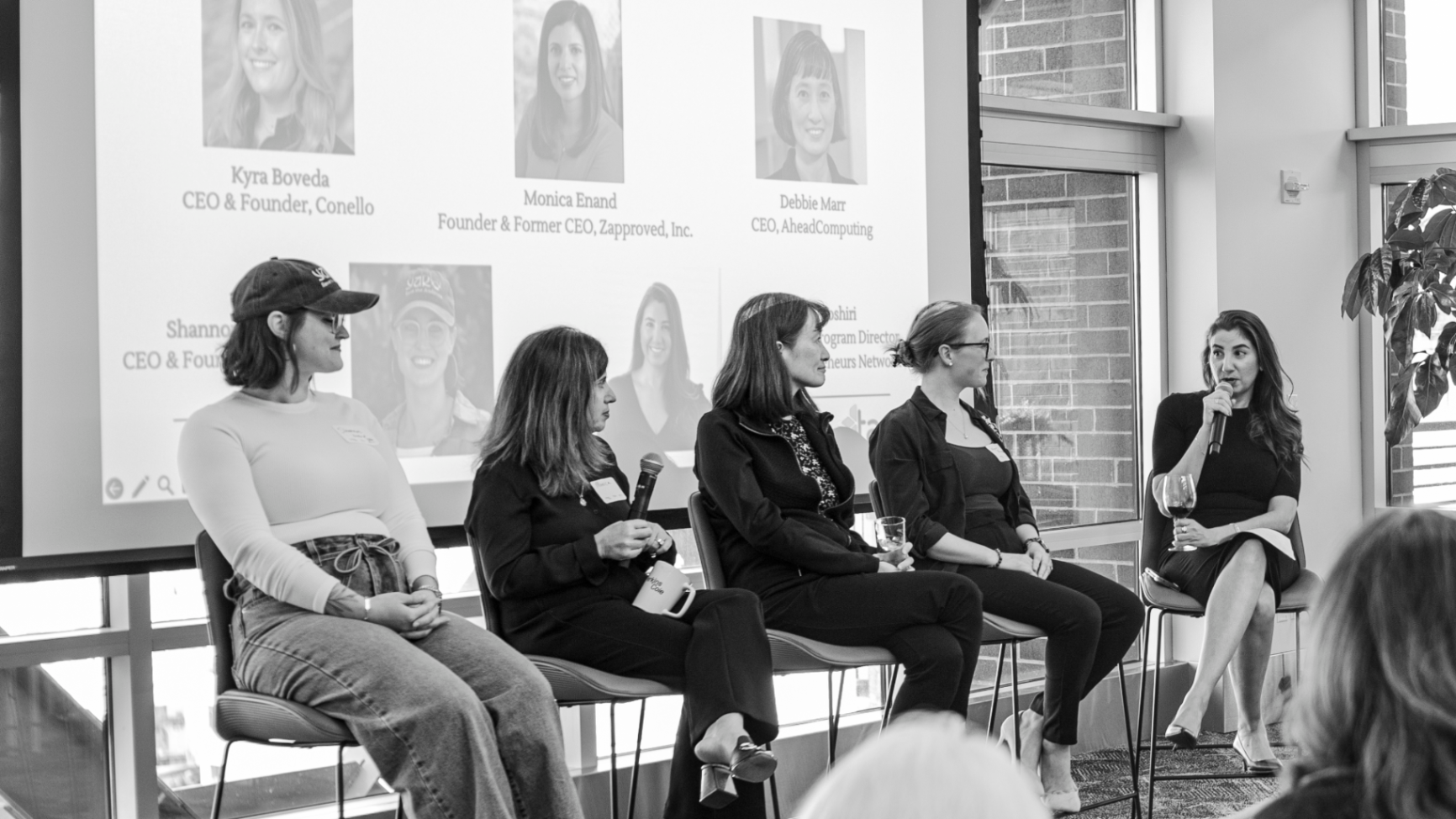 Side view of panelists seated on stage in front of a projected founder panel slide.